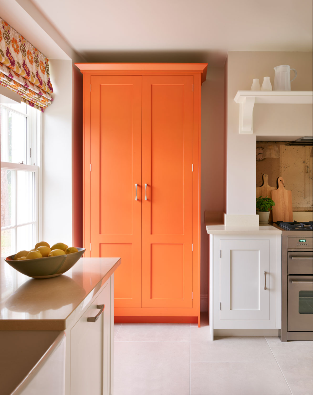 tall orange wardrobe in white kitchen with white large tile floor and orange floral window blinds