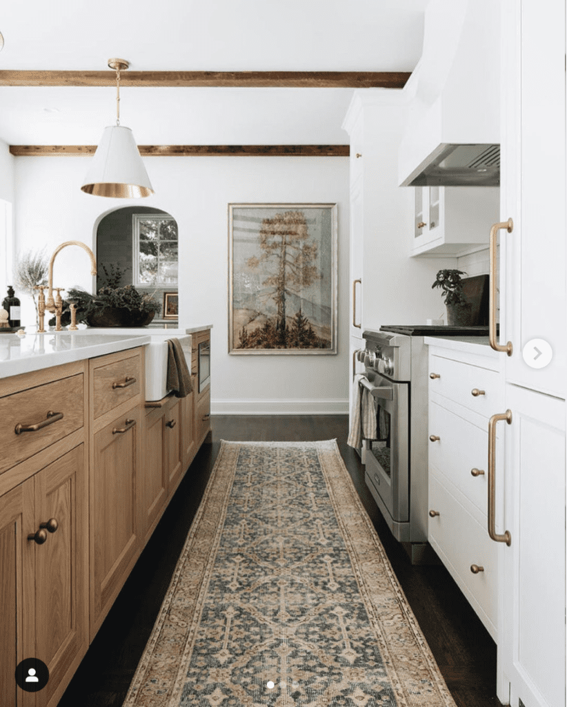 white kitchen with oak island unit, dark hardwood floor, vintage runner rug and vintage tree painting and white marble countertops