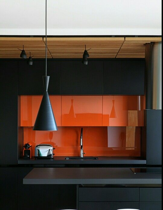 Shiny bright orange kitchen backsplash and black matte cabinetry