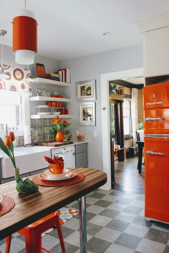 retro style kitchen with orange accents like the fridge, bar stools, blinds, lighting fixtures, vases and placemats. 