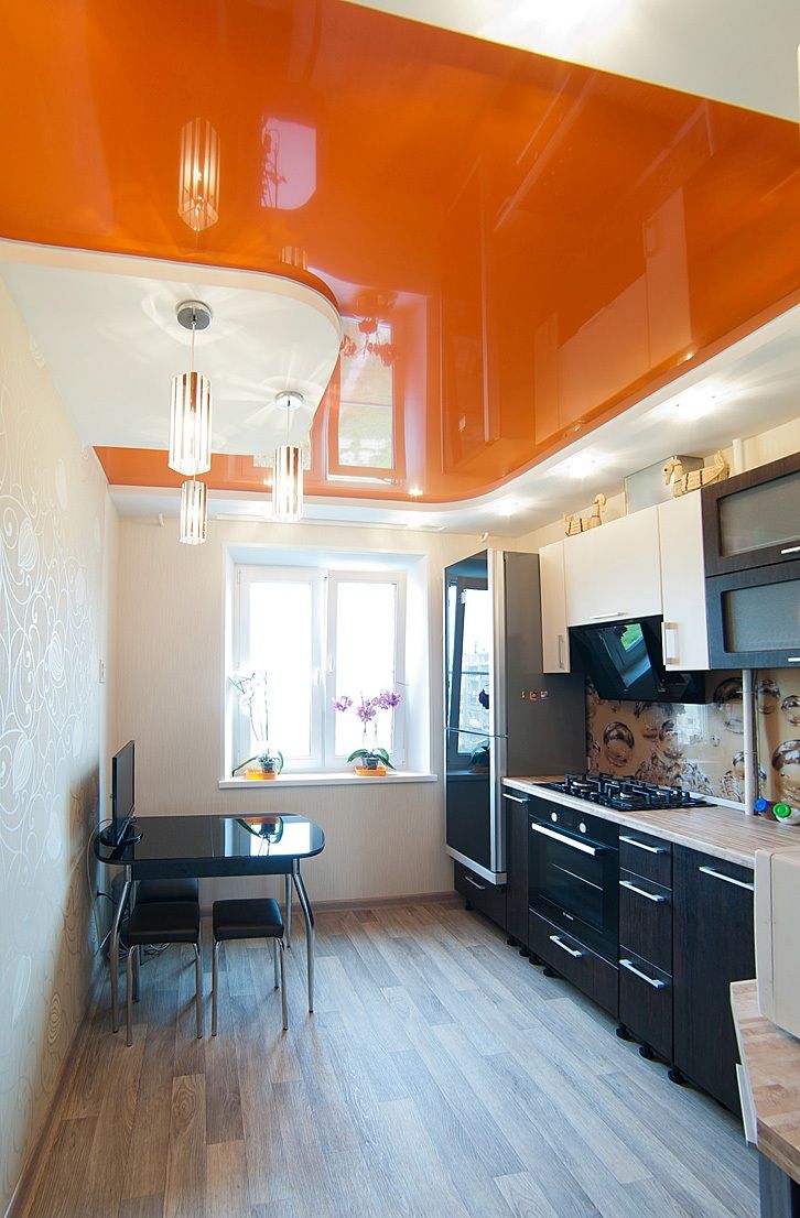 Orange glossy ceiling in black and white kitchen with dark wooden floor.