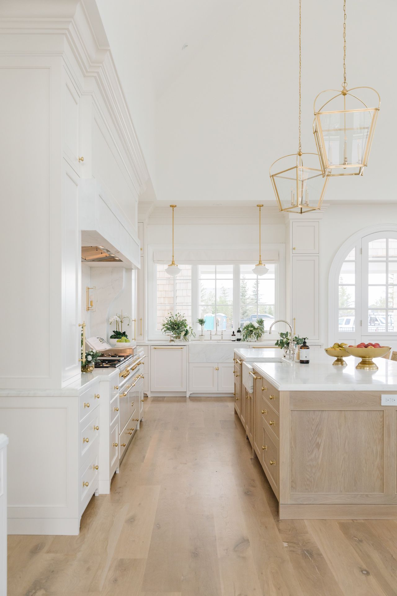 luxurious white kitchen with oak floor and island, gold fixtures and pendant lights and marble worktops