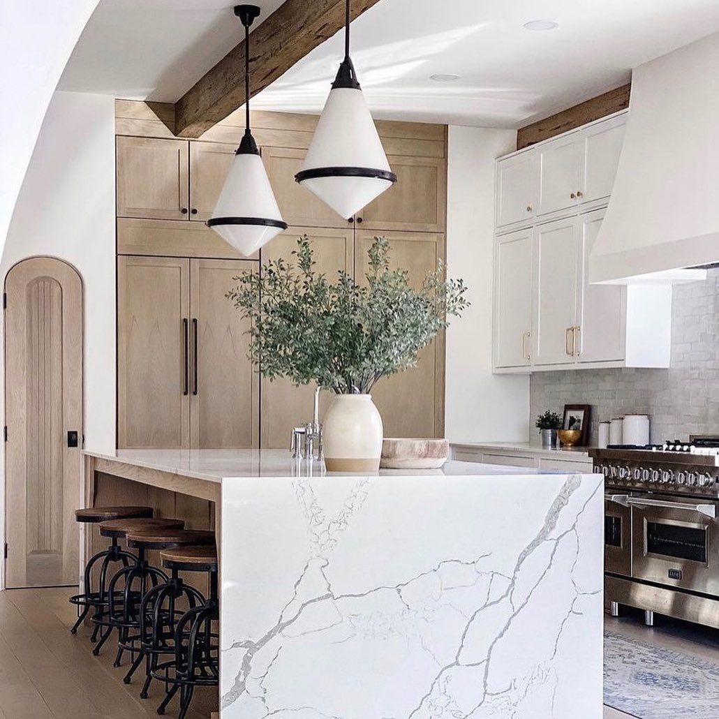 white quartz island unit is oak kitchen with white pendant lights and olive branches in beige vase. 