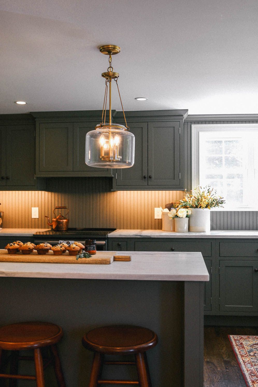 dark green kitchen with warm under counter lighting and glass pendant light over island