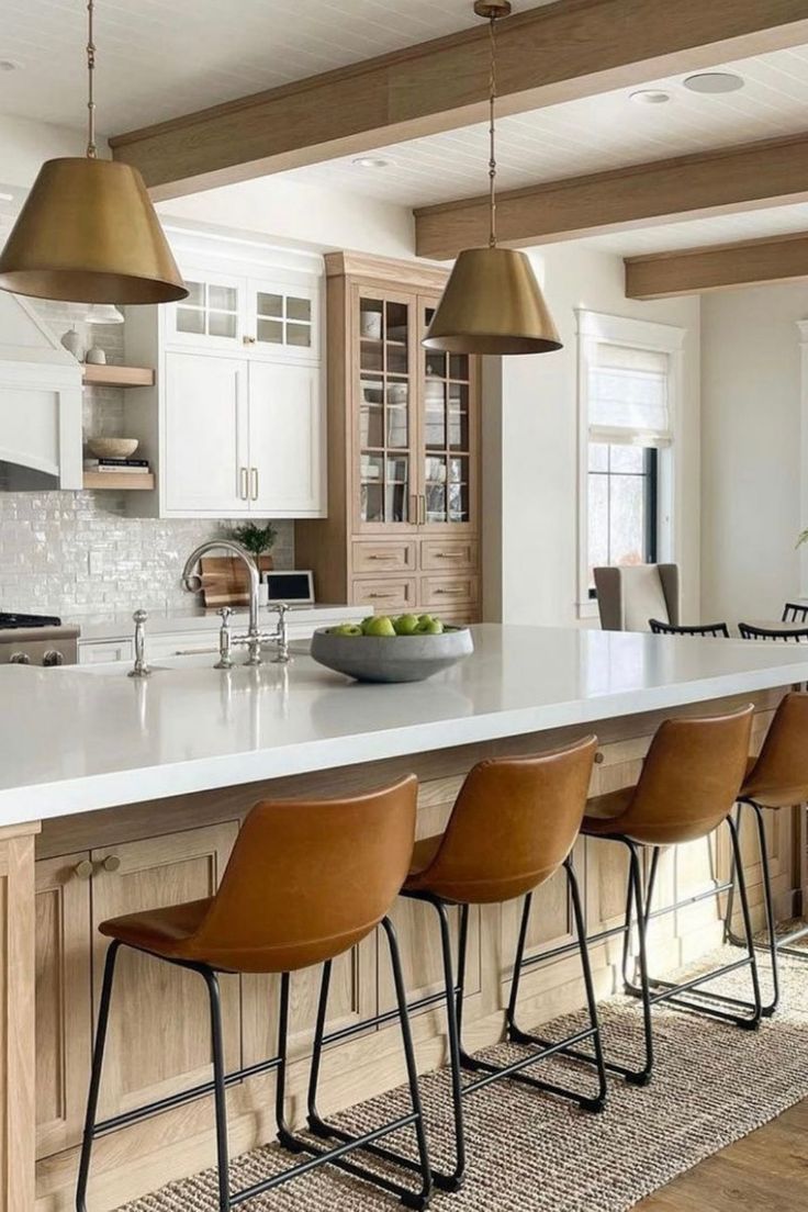 modern kitchen with leather bar stool chairs with black metal legs, white quartz countertops and oak cabinets and floor. brass pendant lights over island.