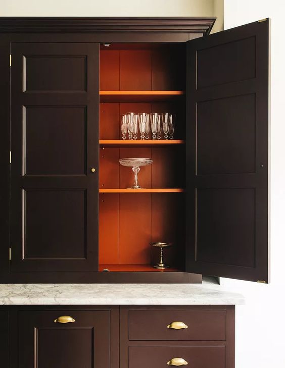 Dark brown kitchen cabinets with orange paneling interior in classic style, brass hardware and marble countertop