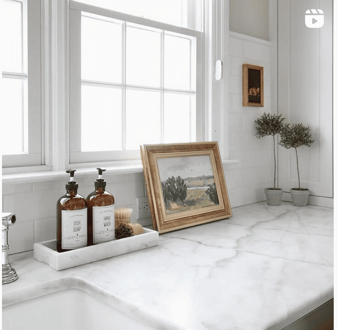 matching vintage hand soap and hand lotion apothecary style, next to golden frame with trees painting on white marble countertop