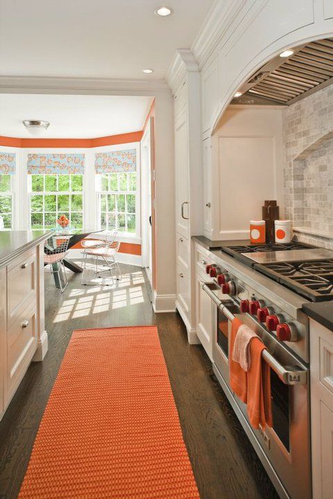 classic white kitchen with orange rug, roman blinds and towels.